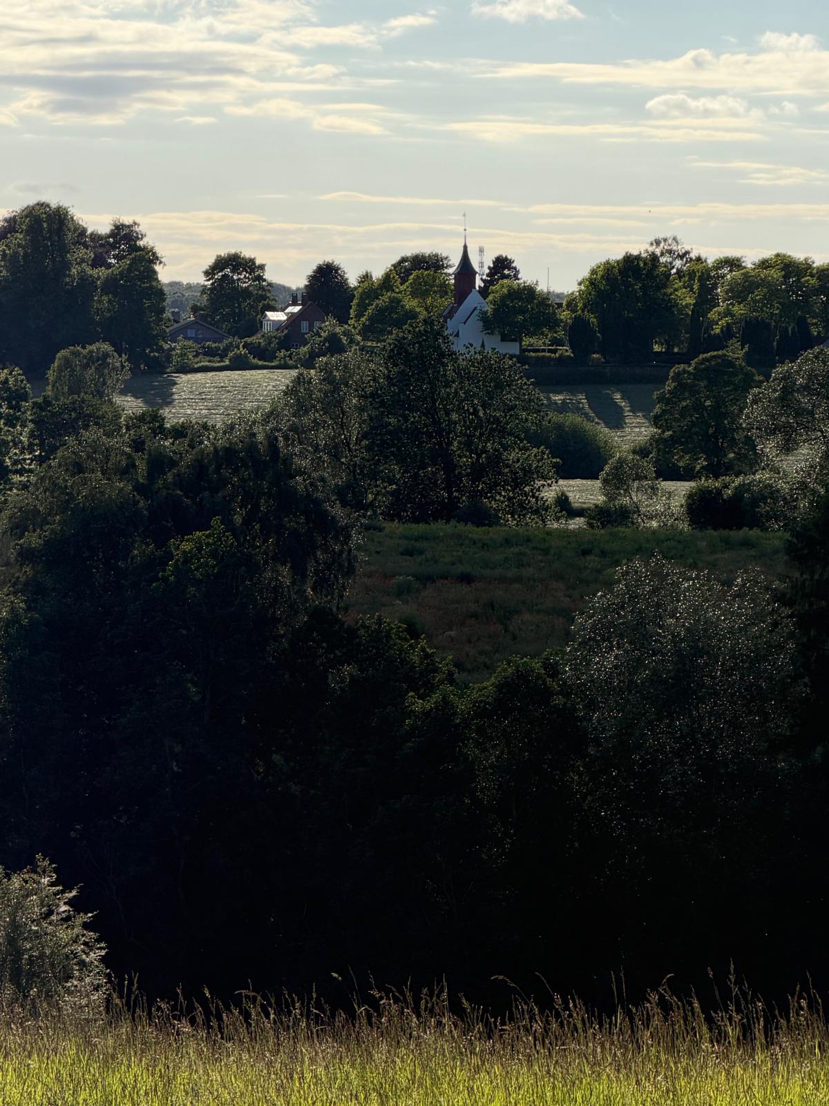 Evening light over fields and trees in Skjoldungernes land, a white church on the ridge